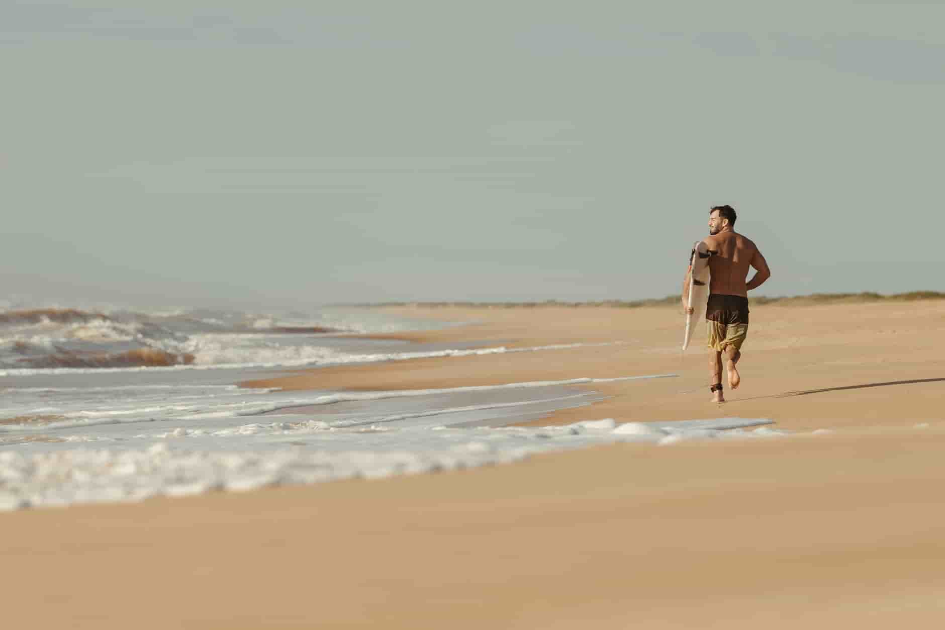 Fitness man running on a beach waves breaking surfer with a surfboard