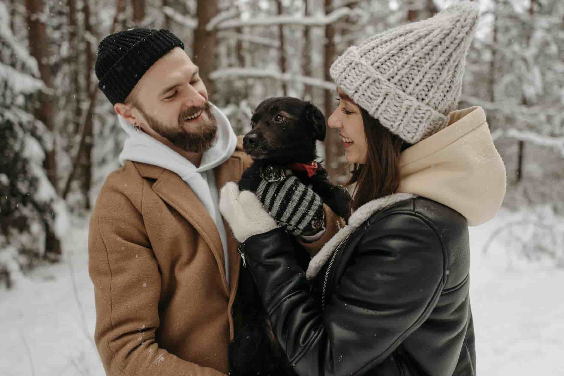Mindset and Health man and woman smiling happy together couple holding a cute black dog in a snowy forest